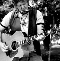 Rusty Bladen playing the harmonica and guitar